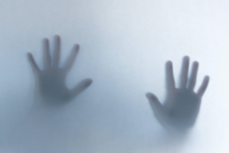 Defocused scary ghost hands behind a white glass background